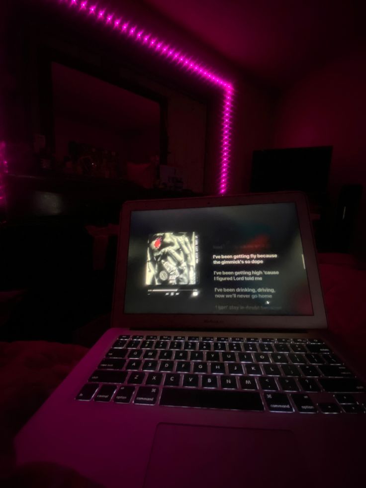 an open laptop computer sitting on top of a bed in a room with purple lighting