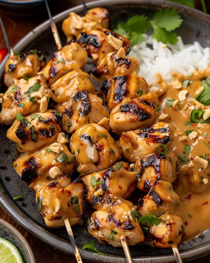 chicken skewers with peanut sauce and white rice on a plate next to lime wedges