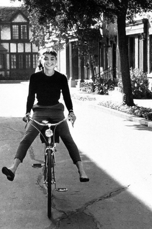 a man riding a bike down a sidewalk next to a tree and building in the background