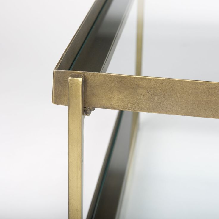 a glass table with brass frame and metal handles on the bottom, against a white background