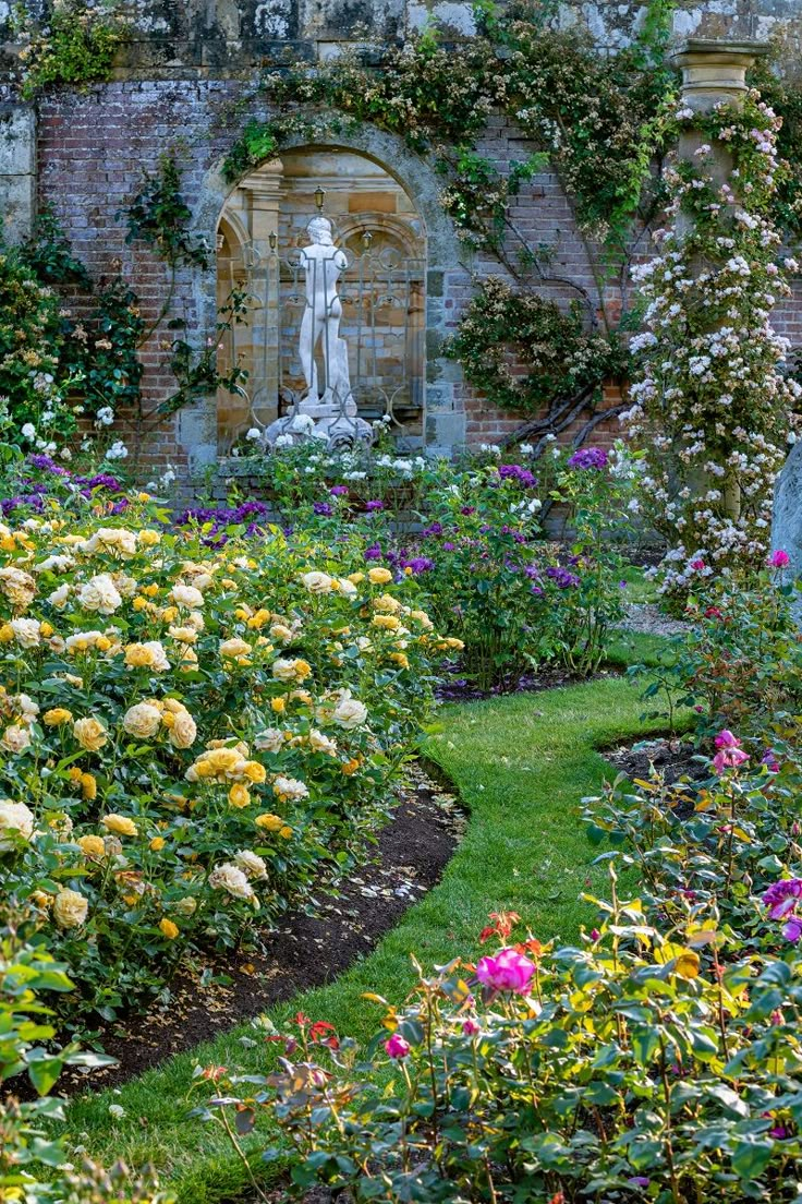 the garden is full of colorful flowers and greenery, with a statue in the background