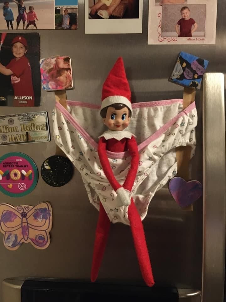 an elf is hanging on the refrigerator door with pictures and magnets all around it