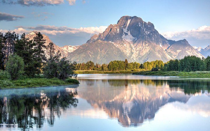 a mountain range is reflected in the still water of a lake surrounded by trees and grass