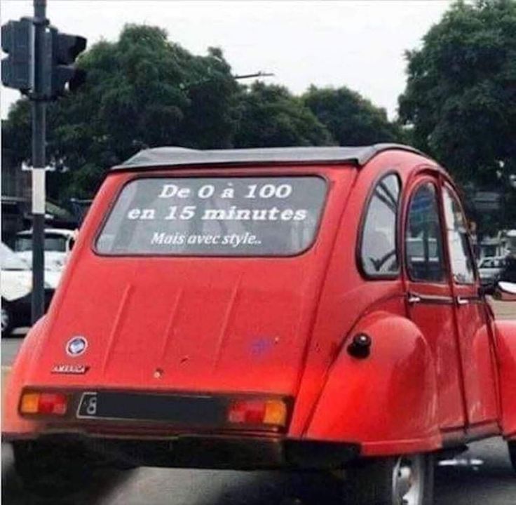 a small red car driving down a street next to a traffic light with trees in the background