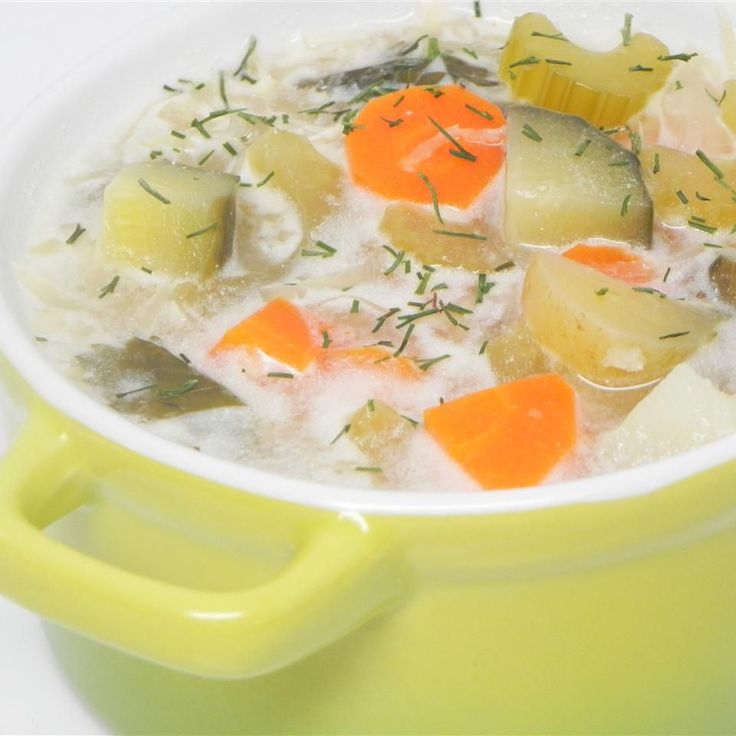 a green pot filled with soup and vegetables on top of a white countertop next to a yellow spoon