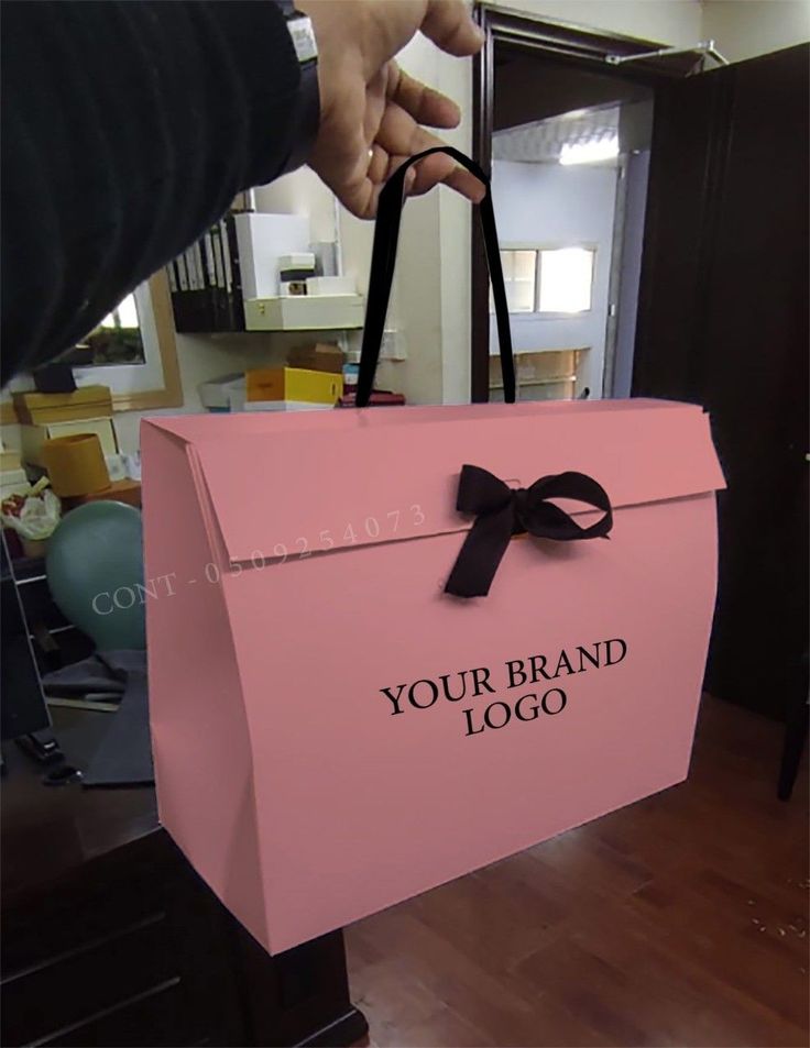 a person is holding a pink bag with a black bow on it that says your brand logo