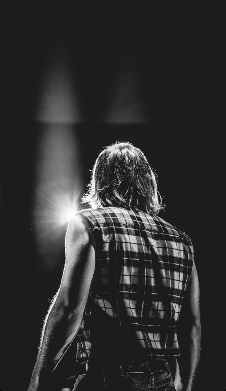 black and white photograph of a man in plaid shirt standing on stage with his back turned to the camera