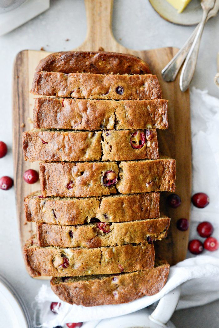 a loaf of fruitcake bread on a cutting board with cranberries around it