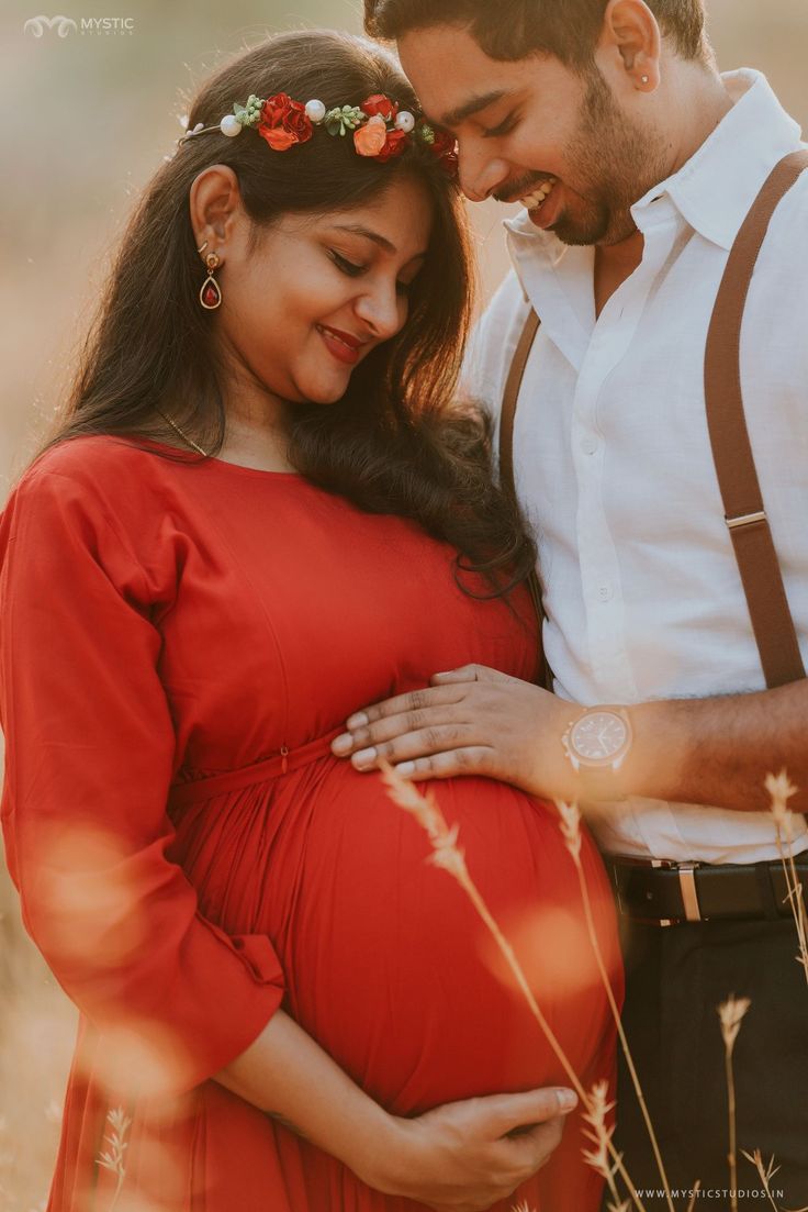 a pregnant woman in a red dress standing next to her husband