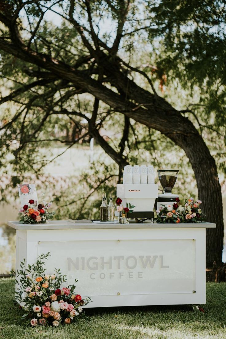 an outdoor bar with flowers and candles on the table in front of a large tree