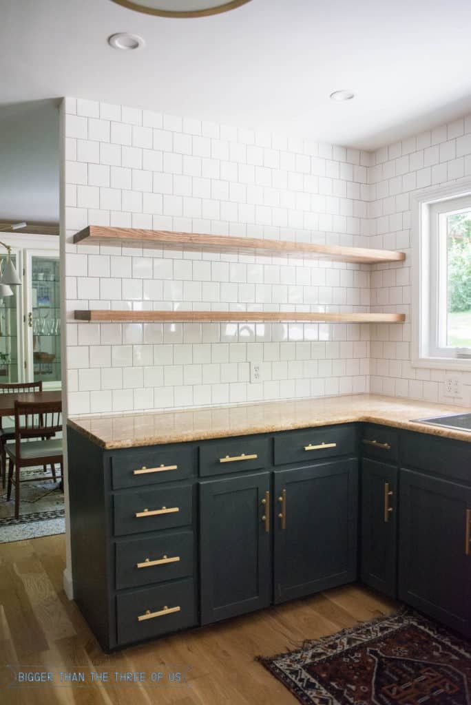 an empty kitchen with black cabinets and white subway tile backsplash, wood flooring