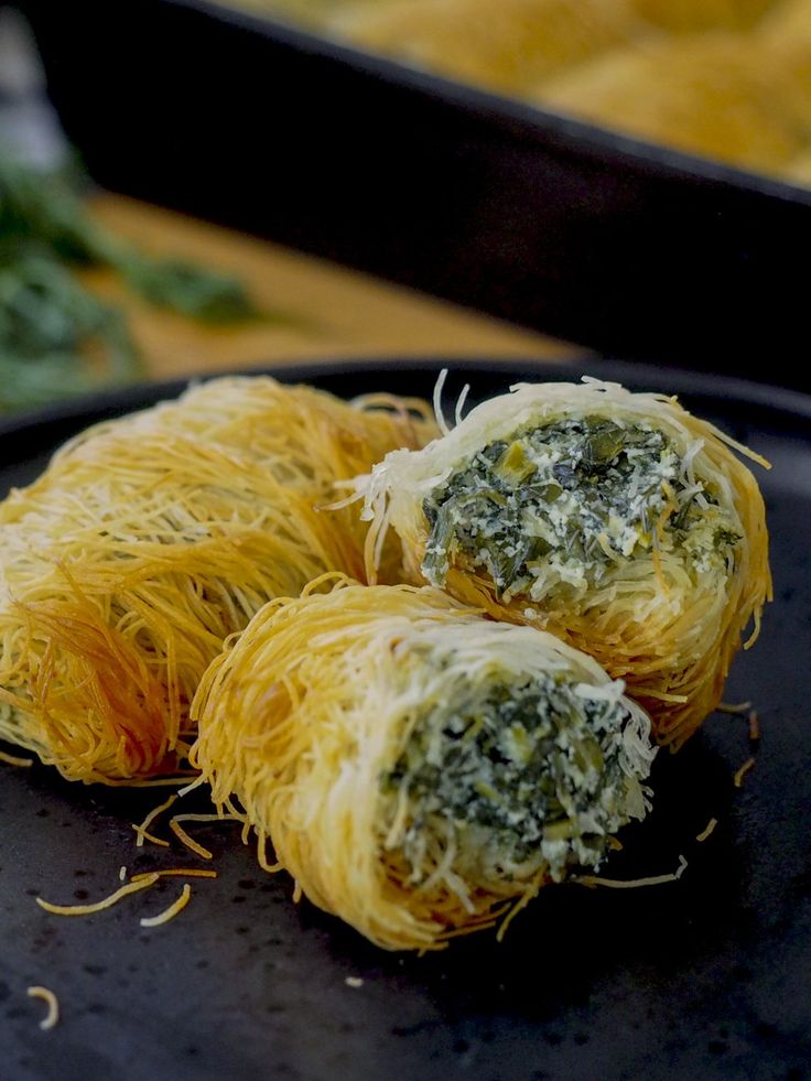 three pieces of food that are on a black plate with cheese and spinach sprinkles