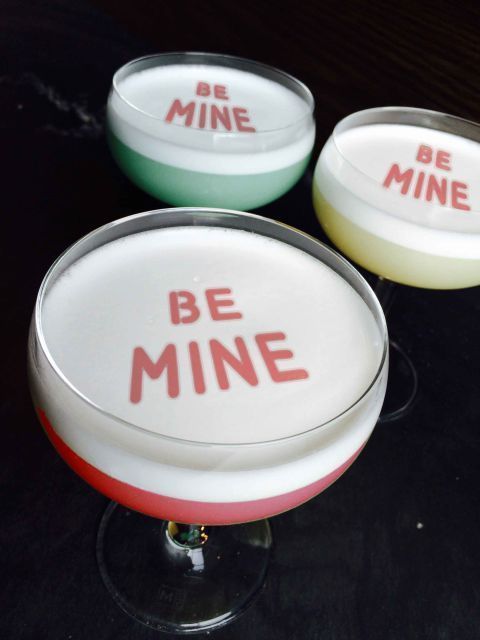 three glasses with different colored drinks in them on a black table top and one has the words be mine written on it