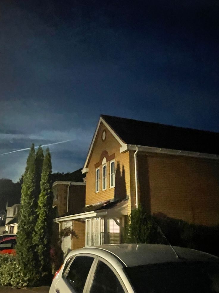 a car is parked in front of a house at night with dark clouds above it