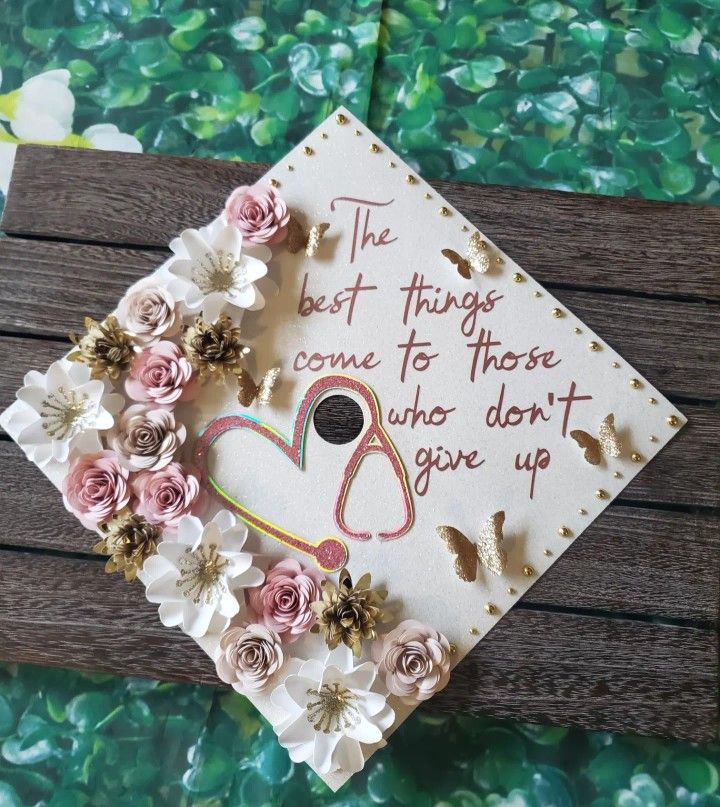 a graduation cap decorated with flowers on top of a wooden table next to a green wall