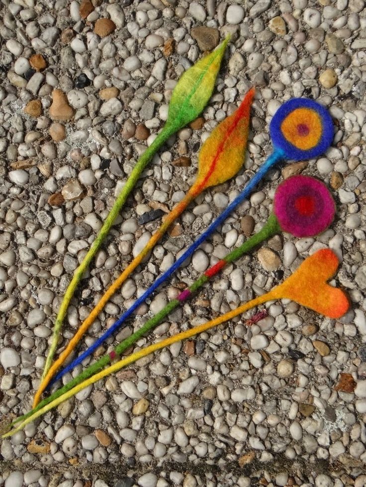 four different colored spoons are laying on the ground next to some rocks and pebbles