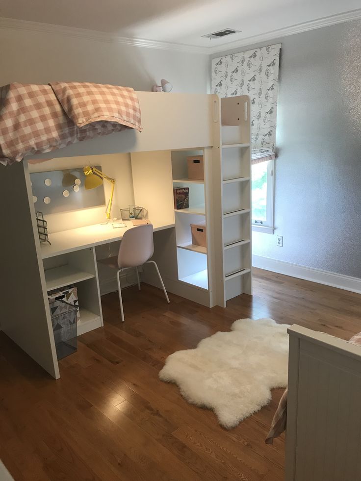 a bedroom with a loft bed, desk and chair next to a white book shelf