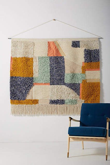 a blue chair sitting in front of a wall hanging with a colorful rug on it