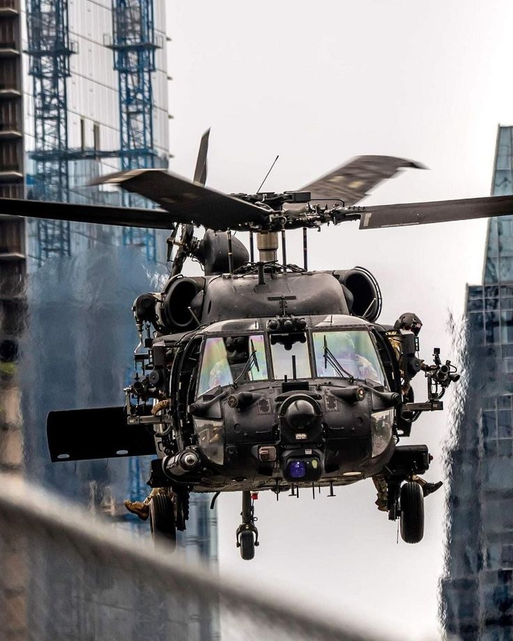 a black helicopter flying through the air near tall buildings