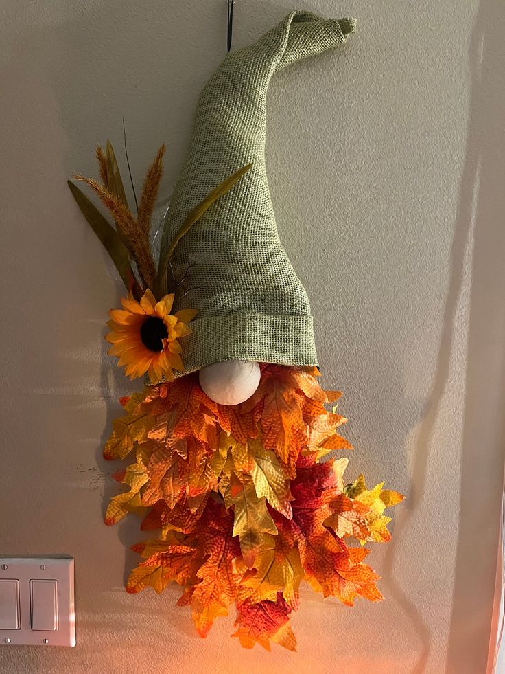 a green knitted hat hanging on the wall with autumn leaves and sunflowers