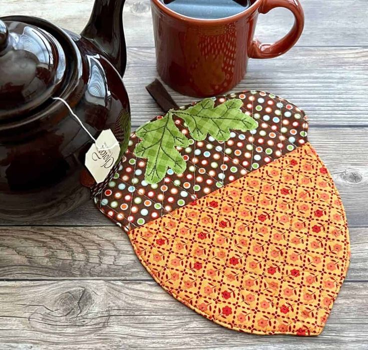 a teapot and cup on a wooden table next to an orange patchwork pot holder