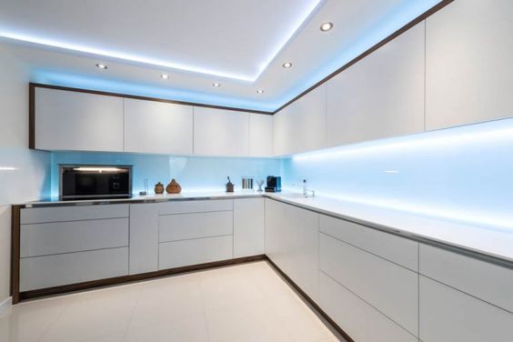 a kitchen with white cabinets and blue lighting on the ceiling is lit by recessed lights