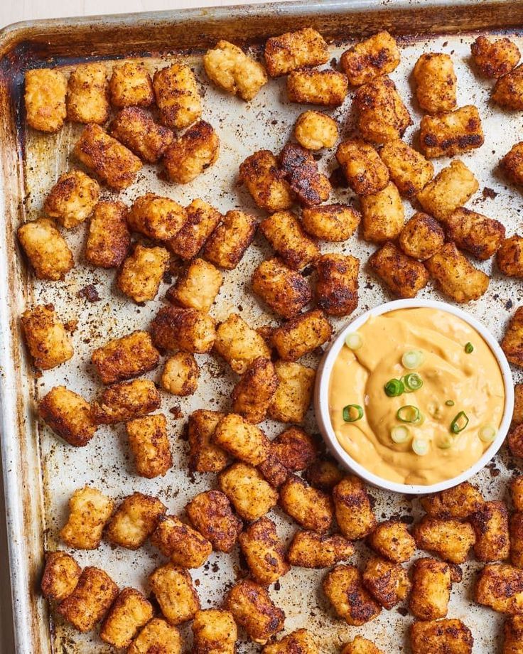 some tater tots are sitting on a baking sheet with a dipping sauce in the middle