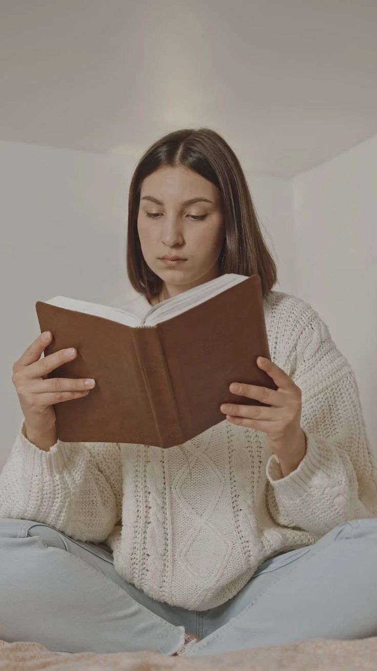 a woman sitting on the bed reading a book