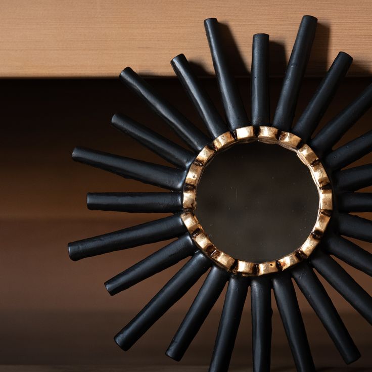 a black and gold sunburst mirror sitting on top of a wooden shelf