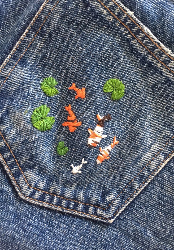 several orange and white fish in the back pocket of a jean jacket with green leaves on it