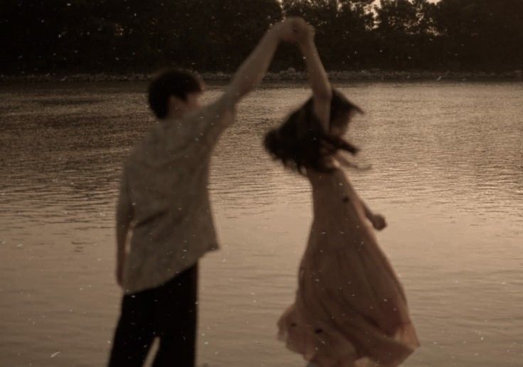 a man and woman are dancing in the water at sunset or sunrise, with trees in the background