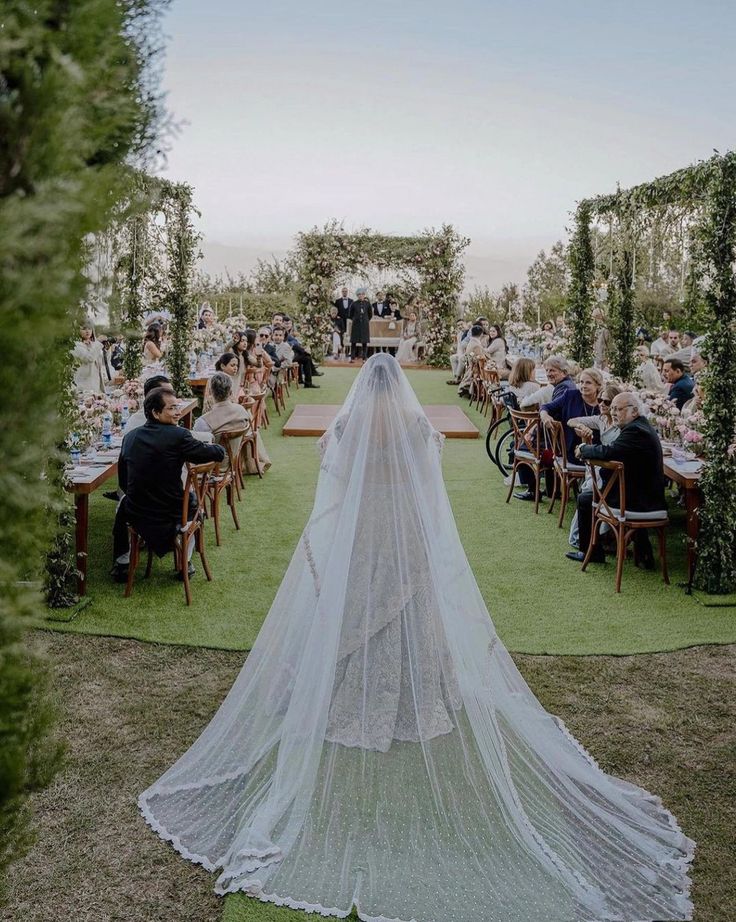 the bride is walking down the aisle with her long veil over her head as she waits to walk down the aisle