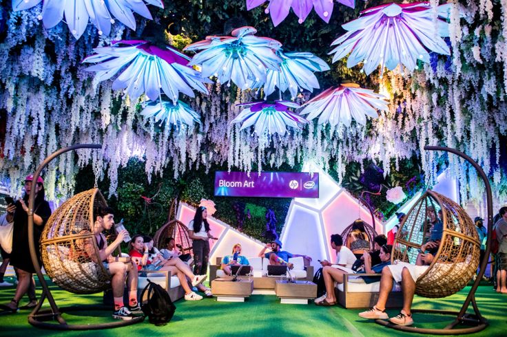 people are sitting in hammock chairs on the green carpeted area with hanging flowers