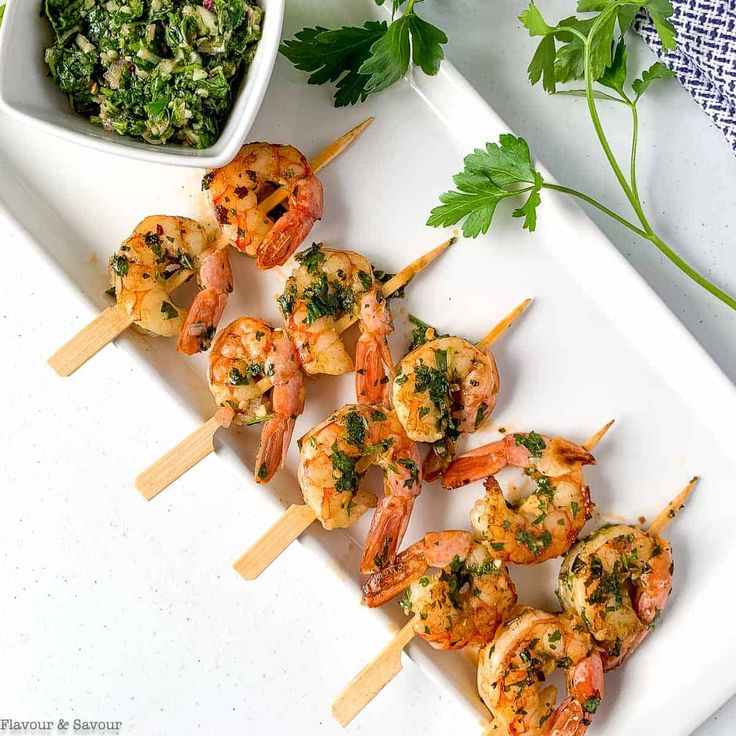 grilled shrimp skewers with pesto and parsley on a white platter