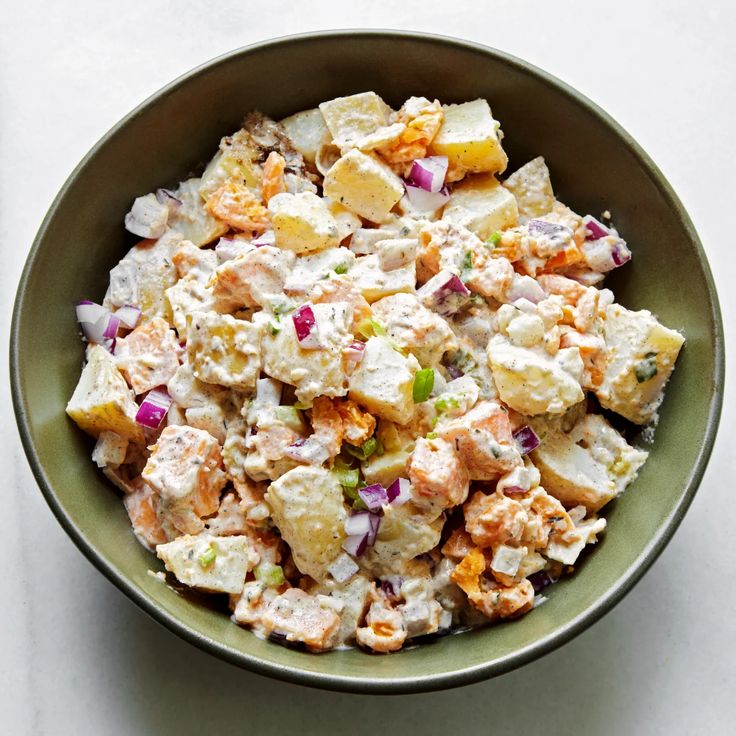 a green bowl filled with potato salad on top of a white countertop next to a fork