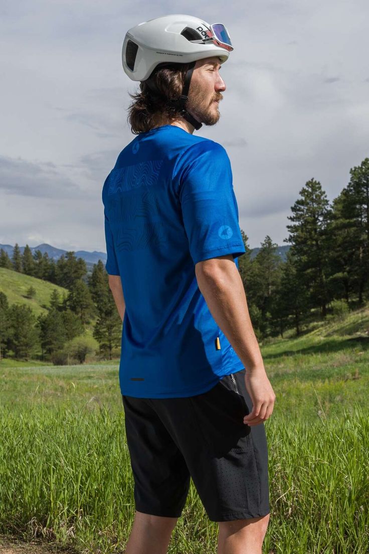 a man wearing a bike helmet standing in the grass with his back to the camera