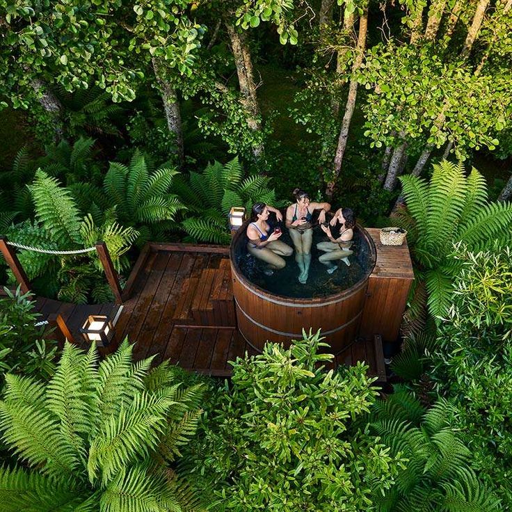 three people in a hot tub surrounded by greenery and trees, with one person sitting on the deck