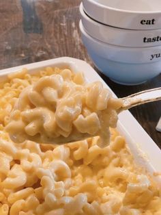 macaroni and cheese is being spooned into a white casserole dish