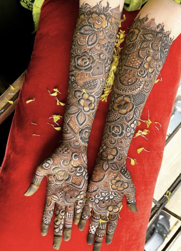 two hands with henna tattoos on them sitting next to each other in front of a red cushion