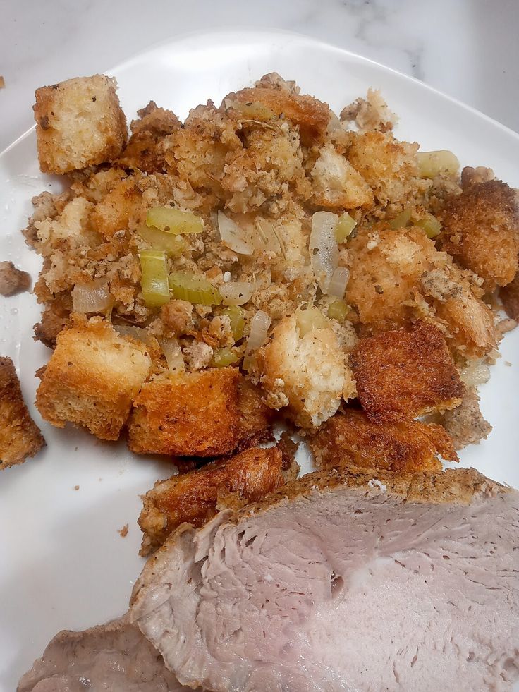 a white plate topped with meat and stuffing next to bread crumbs on top of it