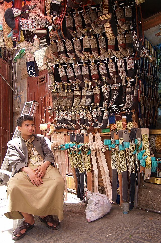 a man sitting in front of a store with lots of shoes hanging on the wall