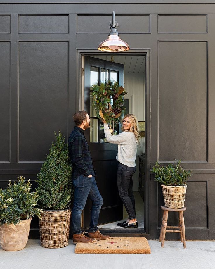 a man and woman standing in an open door to a house with potted plants