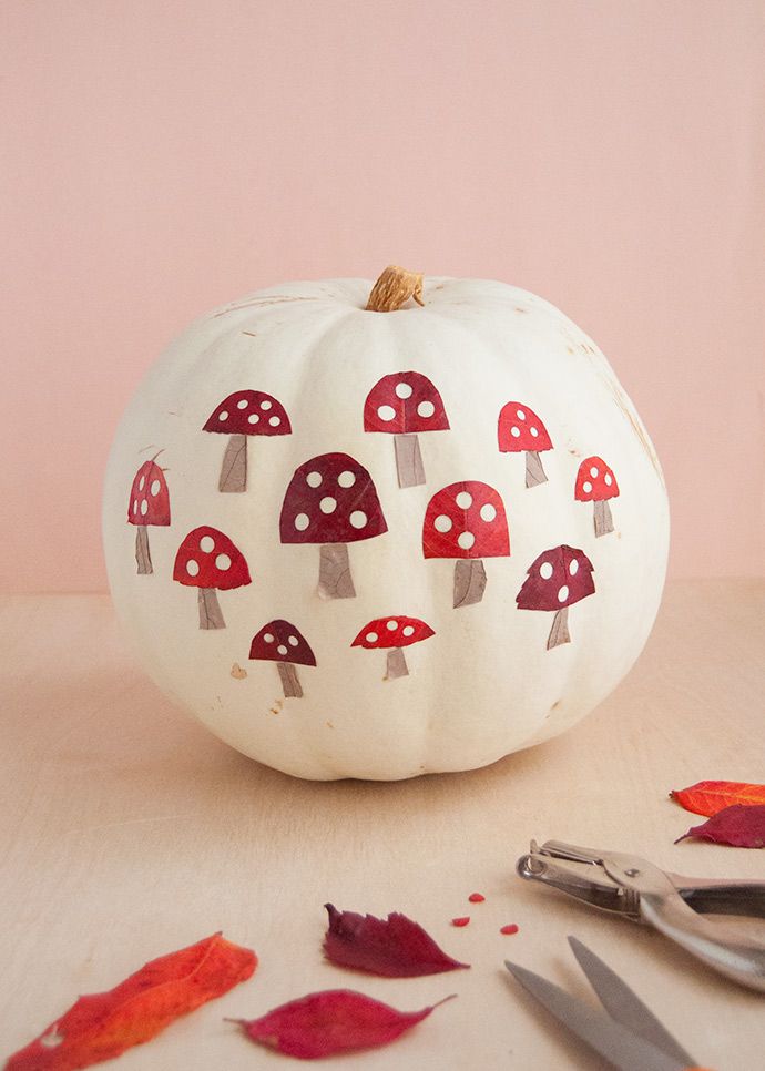 a white pumpkin with red mushrooms painted on it next to scissors and autumn leaf litter