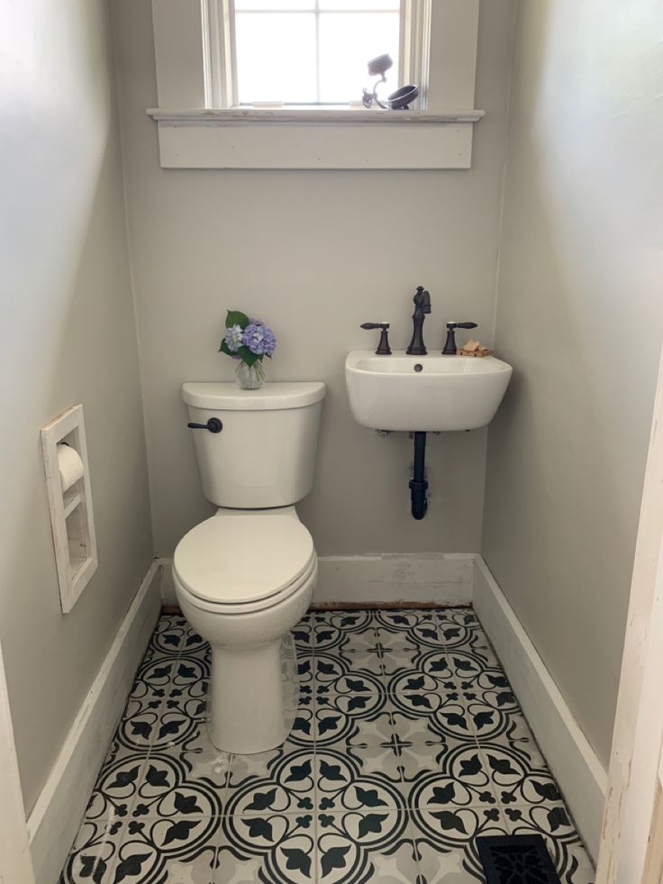 a white toilet sitting next to a sink in a bathroom under a window on top of a tiled floor