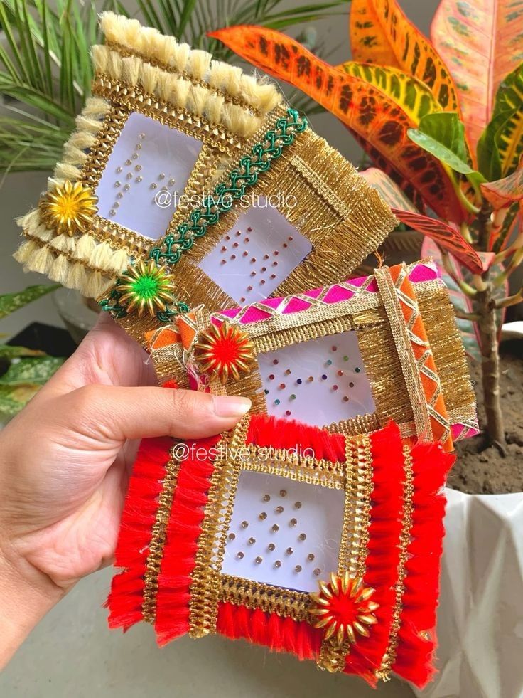 the hand is holding three small pieces of colorful fabric with gold and red trims