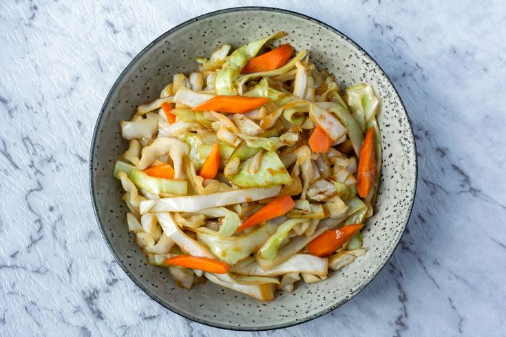 a bowl filled with cabbage and carrots on top of a marble countertop next to a spoon