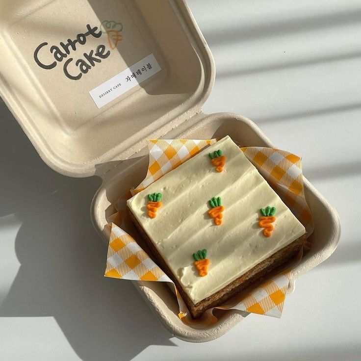 a cake in a box with carrots on it sitting next to an empty container