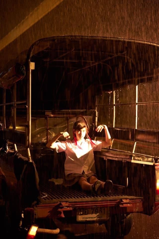 a woman sitting on the back of a truck in the rain with her arms outstretched