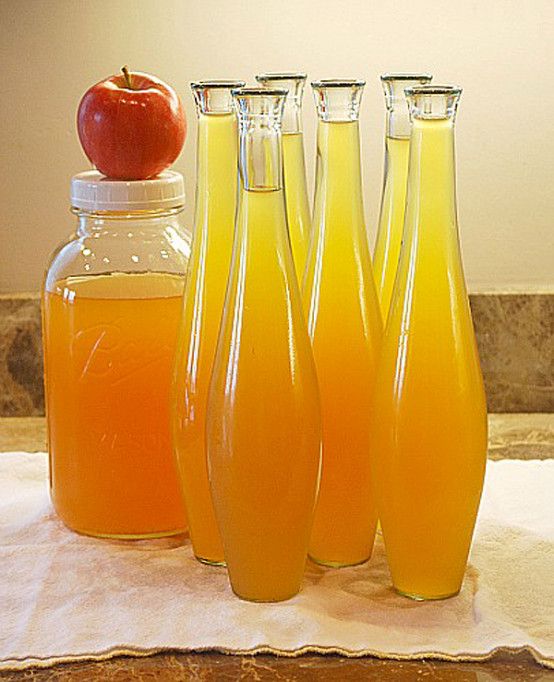 four glass bottles filled with liquid next to an apple on a towel and another bottle full of orange juice