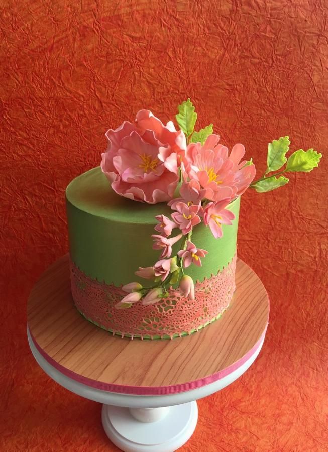 there is a green cake with pink flowers on the top and bottom, sitting on a stand